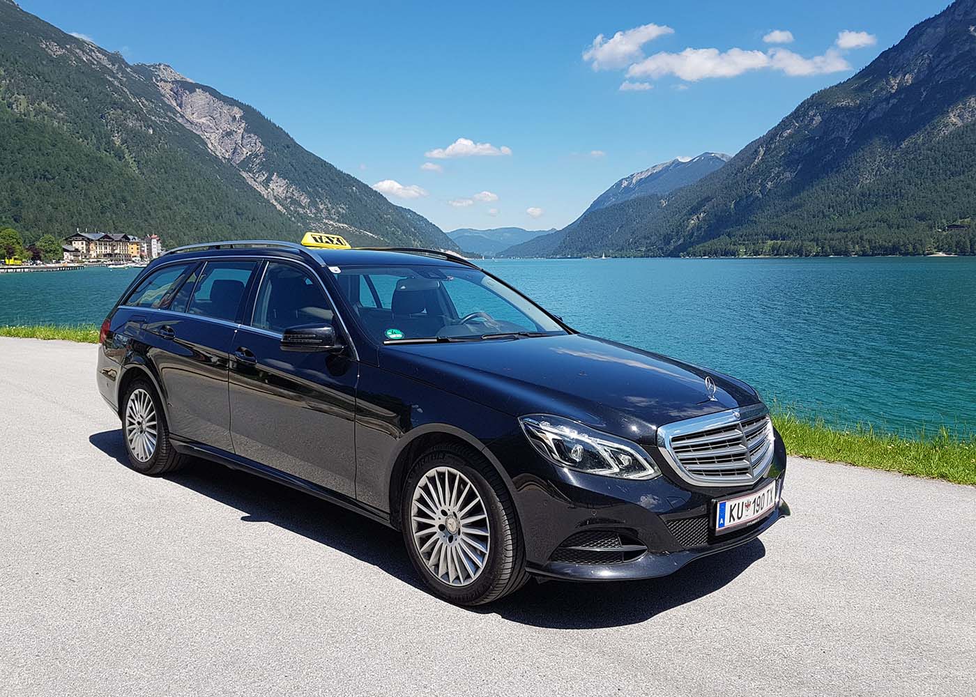 Taxi von Gabriel Moser auf einer Straße mit einer Berglandschaft mit See im Hintergrund